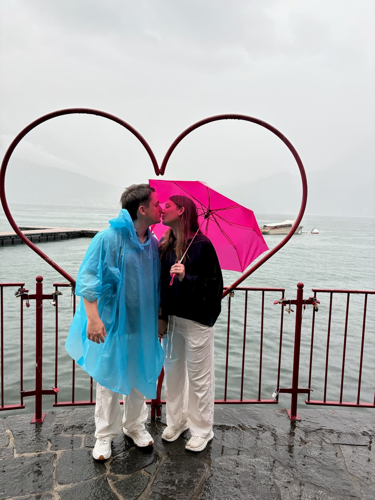 Kissing in the rain at a lakeside heart sculpture